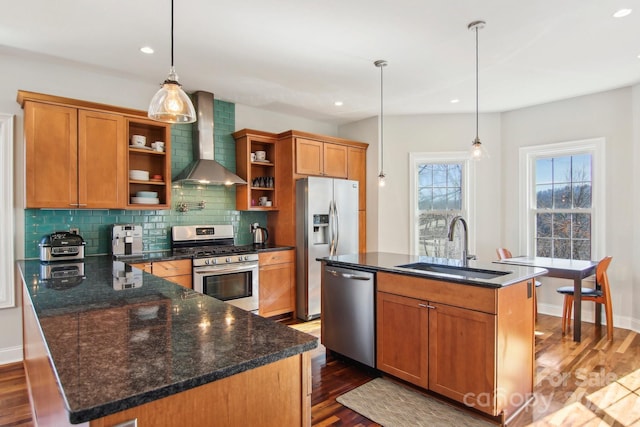 kitchen featuring stainless steel appliances, a kitchen island with sink, hanging light fixtures, and wall chimney range hood