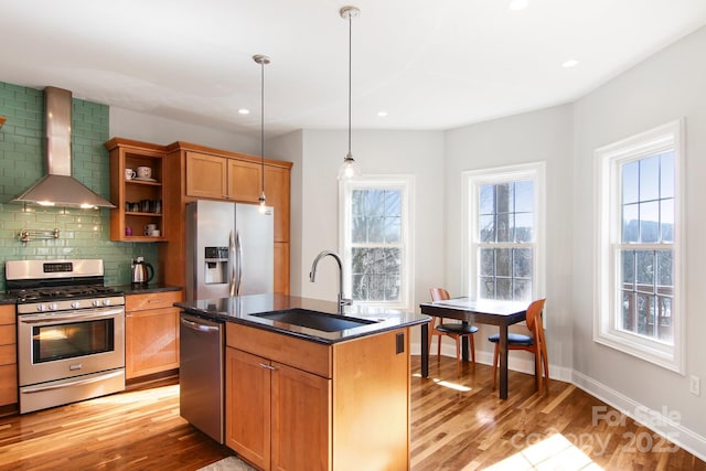 kitchen with wall chimney exhaust hood, sink, tasteful backsplash, appliances with stainless steel finishes, and an island with sink