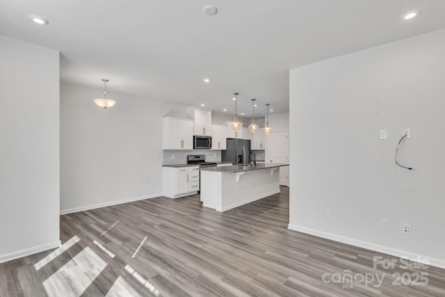 kitchen featuring appliances with stainless steel finishes, an island with sink, hanging light fixtures, and white cabinets