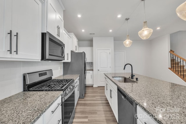 kitchen with sink, light stone counters, appliances with stainless steel finishes, pendant lighting, and white cabinets