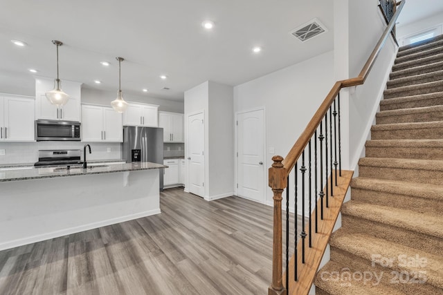 kitchen featuring sink, appliances with stainless steel finishes, white cabinets, decorative light fixtures, and dark stone counters