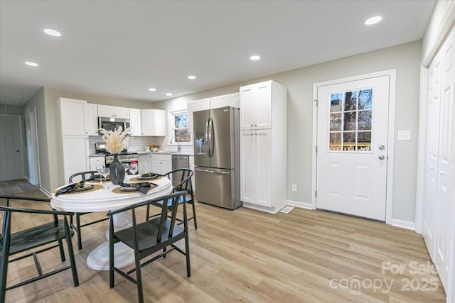 kitchen with tasteful backsplash, light wood-type flooring, white cabinets, and appliances with stainless steel finishes