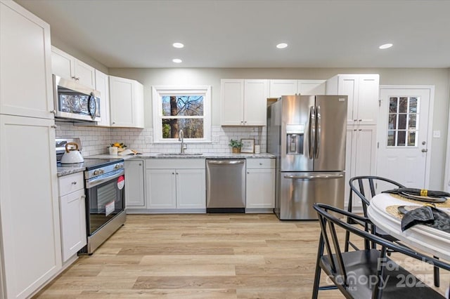 kitchen featuring sink, white cabinetry, stainless steel appliances, light stone counters, and light wood-type flooring