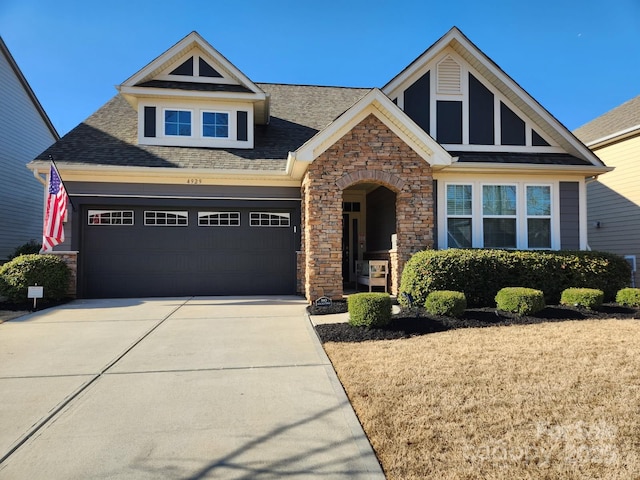 craftsman inspired home with a garage, stone siding, driveway, and a shingled roof