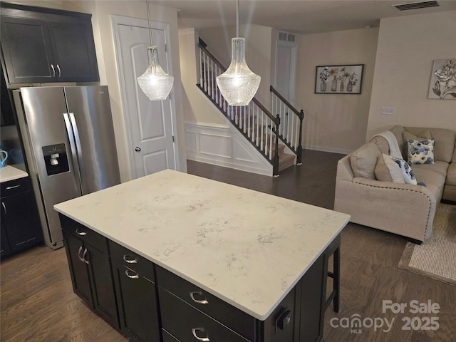 kitchen featuring dark wood finished floors, open floor plan, a kitchen island, dark cabinetry, and stainless steel fridge with ice dispenser