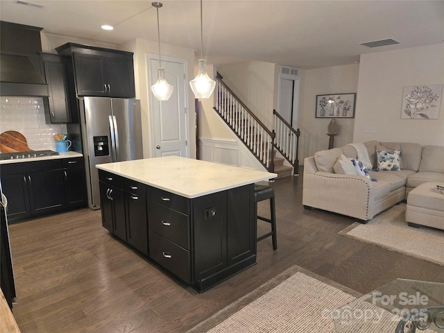 kitchen featuring stainless steel appliances, a breakfast bar, open floor plan, dark cabinetry, and dark wood-style floors