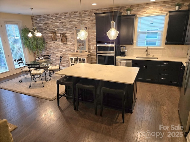 kitchen featuring stainless steel appliances, dark cabinetry, light countertops, a kitchen bar, and a sink