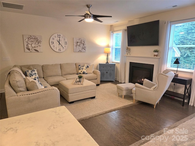 living area featuring a glass covered fireplace, visible vents, ceiling fan, and wood finished floors