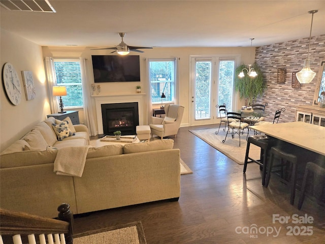 living area with a glass covered fireplace, a healthy amount of sunlight, visible vents, and dark wood-style flooring