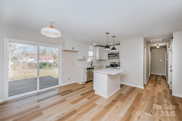 kitchen with white cabinets, a kitchen island, appliances with stainless steel finishes, light countertops, and pendant lighting