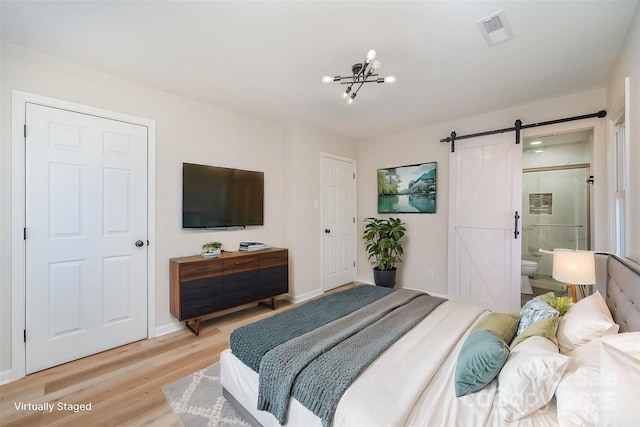 bedroom featuring a barn door, a chandelier, connected bathroom, and light hardwood / wood-style floors