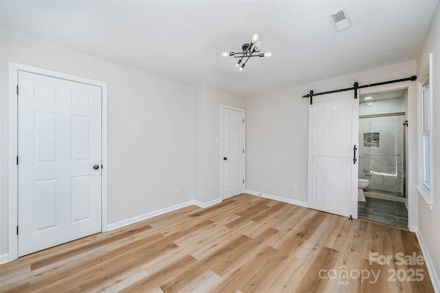 unfurnished bedroom featuring a barn door, a chandelier, connected bathroom, and light wood-type flooring