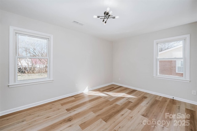 empty room featuring a notable chandelier and light wood-type flooring