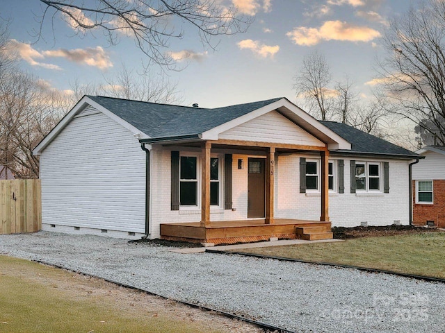 view of front of home with brick siding, a porch, a shingled roof, crawl space, and fence