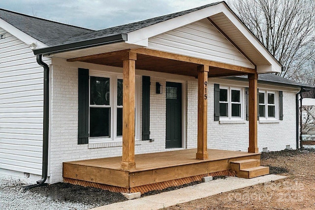 doorway to property featuring a porch, crawl space, a shingled roof, and brick siding