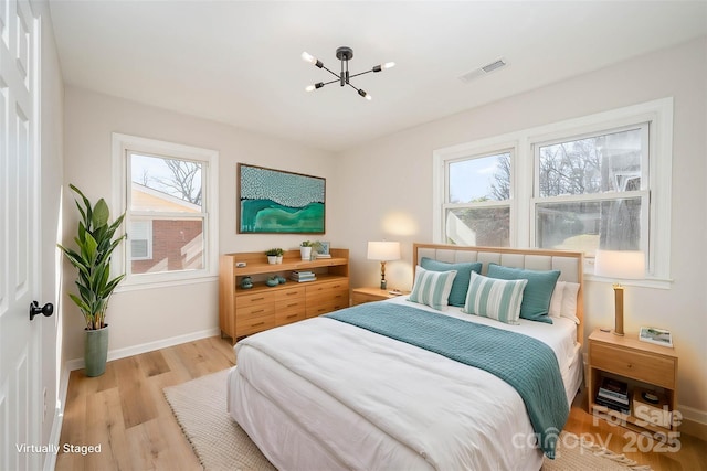 bedroom with a chandelier, light wood finished floors, visible vents, and baseboards