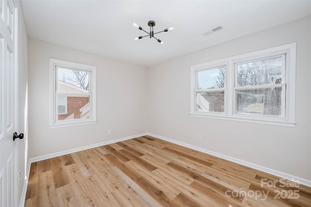 spare room with light wood-type flooring, visible vents, baseboards, and a chandelier