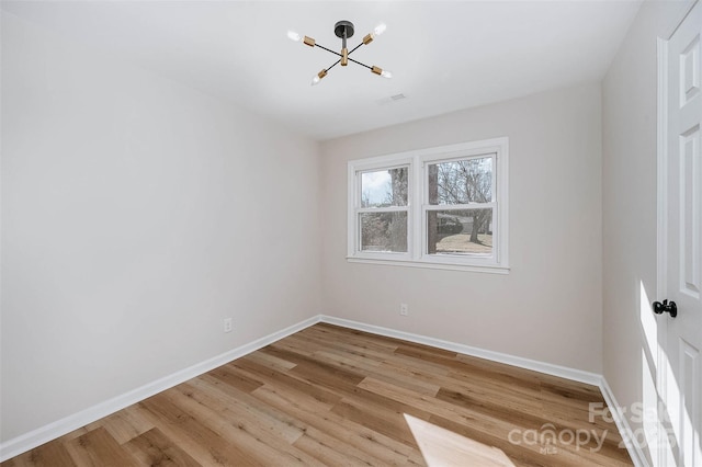 spare room featuring light wood finished floors, baseboards, and a chandelier