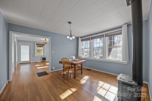 dining space featuring hardwood / wood-style flooring, a wood stove, and an inviting chandelier