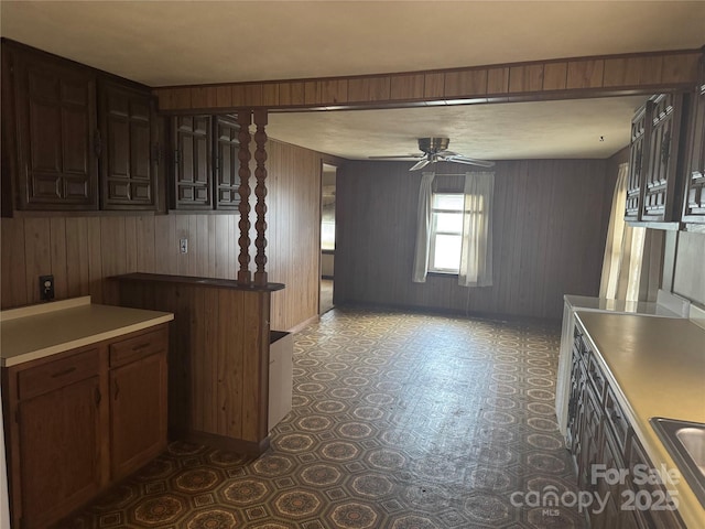 kitchen featuring ceiling fan, sink, dark brown cabinets, and wood walls