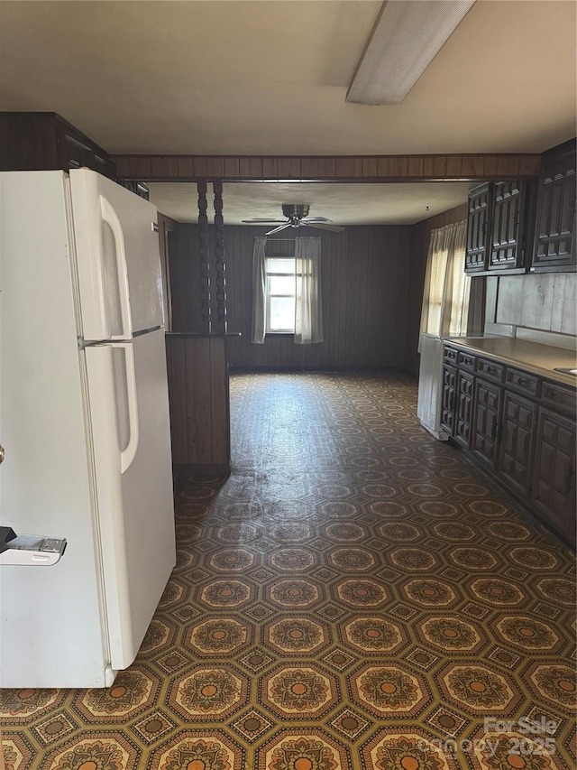 kitchen with white refrigerator, ceiling fan, dark brown cabinetry, and wood walls