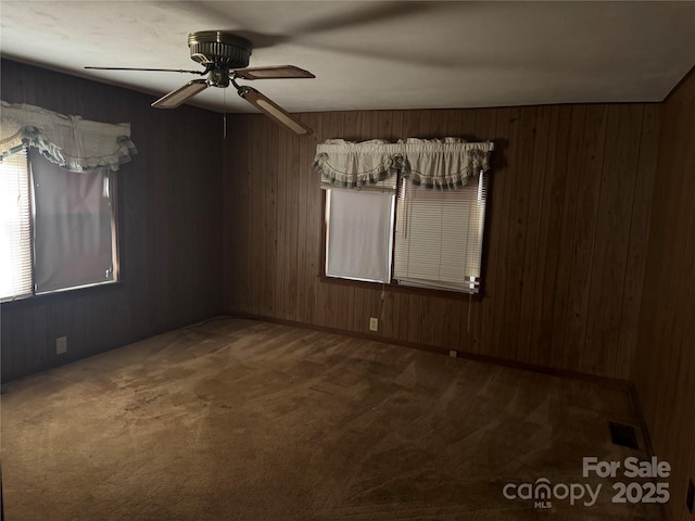 unfurnished room featuring ceiling fan, wooden walls, and dark carpet