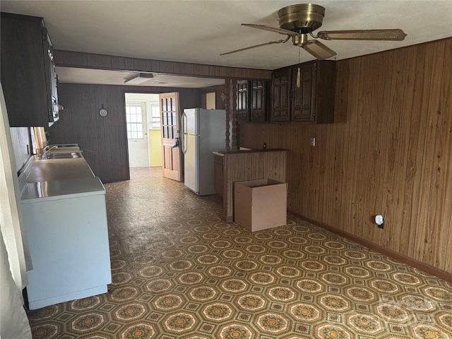 kitchen with fridge, ceiling fan, dark brown cabinetry, and wooden walls