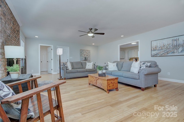 living room featuring ceiling fan, light hardwood / wood-style floors, and a brick fireplace