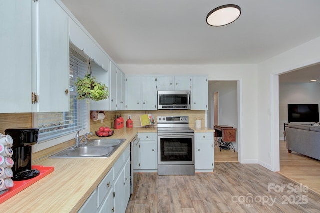 kitchen featuring sink, tasteful backsplash, white cabinetry, light wood-type flooring, and appliances with stainless steel finishes