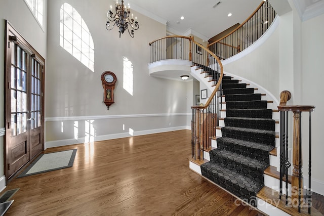 entryway featuring an inviting chandelier, a towering ceiling, dark wood-type flooring, and ornamental molding