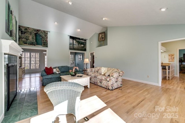 living room featuring high vaulted ceiling, a tile fireplace, and light hardwood / wood-style flooring