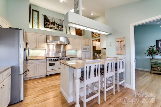 kitchen with wall chimney range hood, a breakfast bar, appliances with stainless steel finishes, a high ceiling, and light stone counters