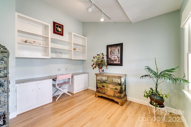 office space featuring lofted ceiling, built in desk, and light hardwood / wood-style floors