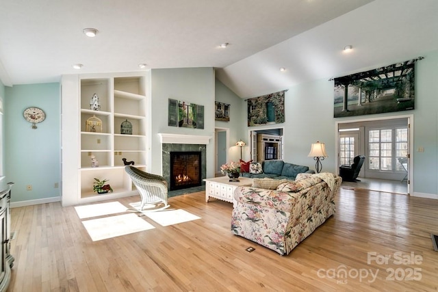 living room with a fireplace, high vaulted ceiling, built in features, and light wood-type flooring