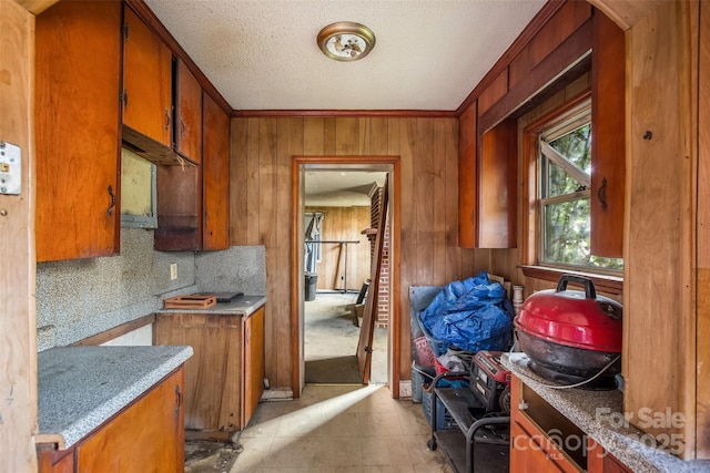 kitchen featuring wooden walls, decorative backsplash, ornamental molding, light tile patterned floors, and a textured ceiling