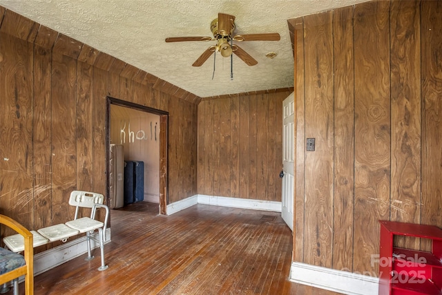 interior space featuring ceiling fan, dark hardwood / wood-style floors, a textured ceiling, and wood walls