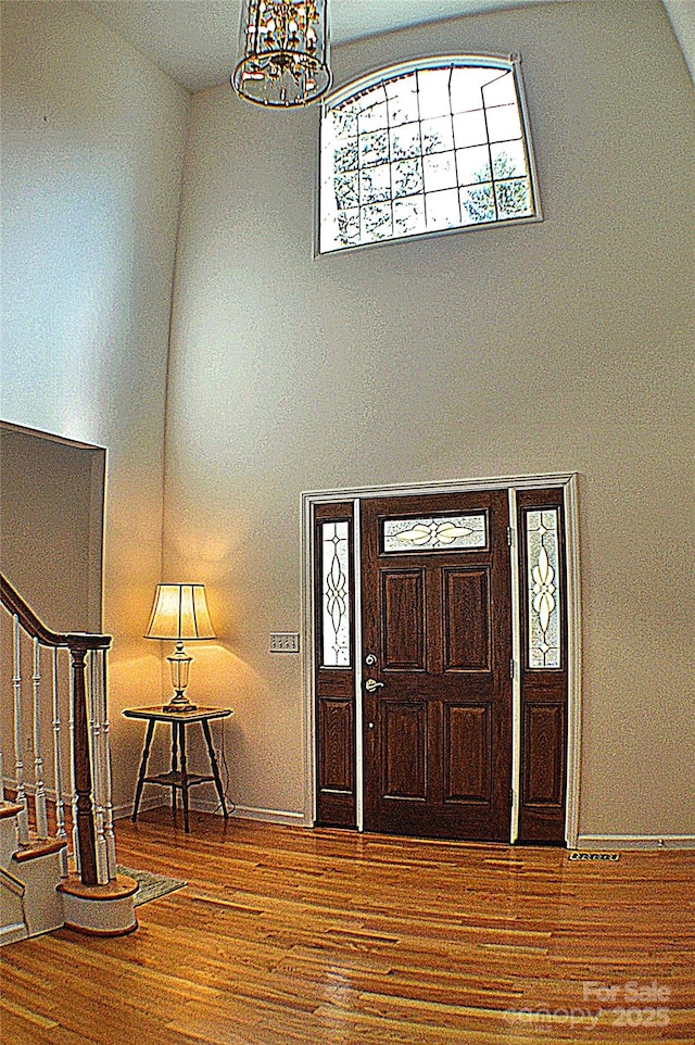 foyer with wood-type flooring, high vaulted ceiling, and a chandelier