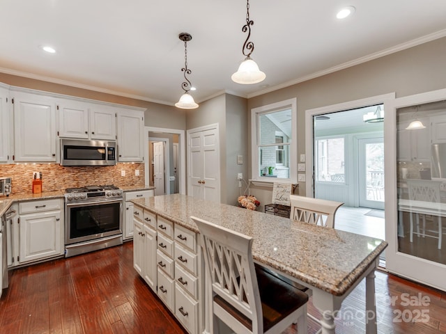 kitchen with pendant lighting, white cabinetry, stainless steel appliances, a center island, and a kitchen bar