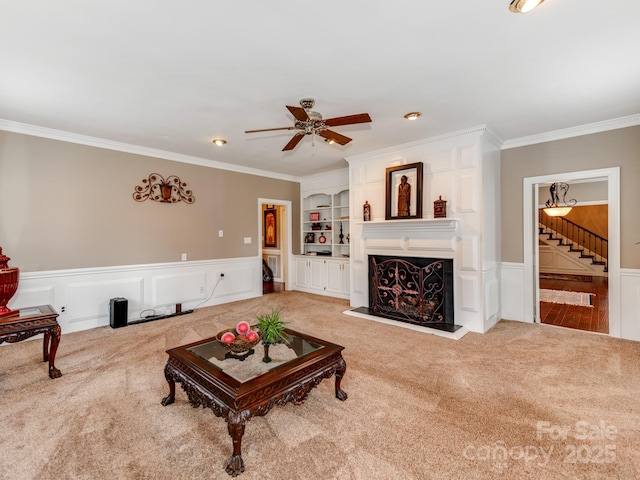 carpeted living room with crown molding, ceiling fan, and built in shelves