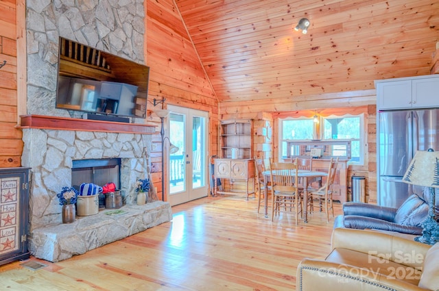 living room with high vaulted ceiling, light hardwood / wood-style floors, a stone fireplace, wooden ceiling, and french doors