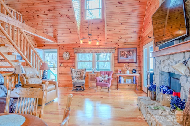 living room with wood ceiling, wooden walls, a stone fireplace, and light hardwood / wood-style floors