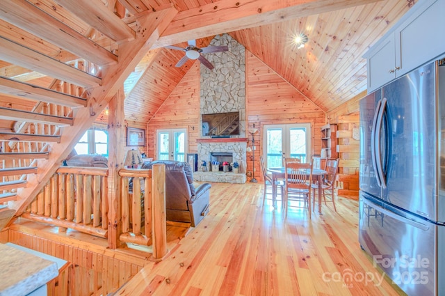 living room featuring a fireplace, wood walls, beamed ceiling, light hardwood / wood-style floors, and french doors