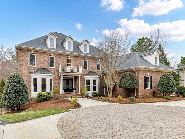 colonial house featuring a balcony, french doors, brick siding, and roof with shingles