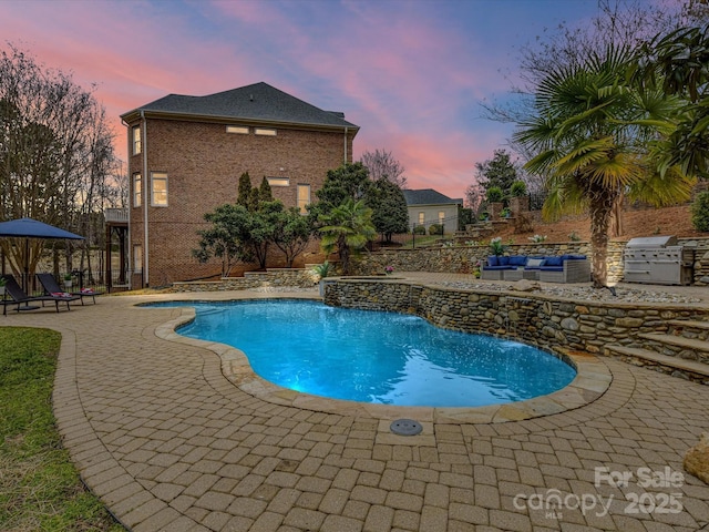 pool at dusk with a patio, an outdoor kitchen, an outdoor living space, an outdoor pool, and grilling area