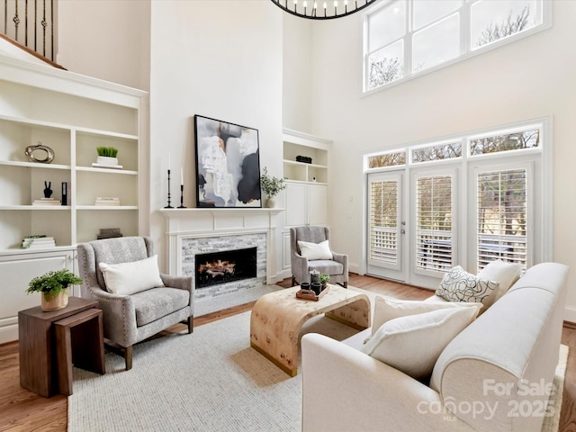 living room featuring a high ceiling, a stone fireplace, wood finished floors, and an inviting chandelier