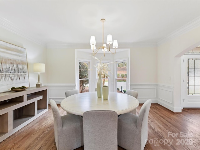 dining space featuring wood finished floors, a wainscoted wall, a chandelier, and ornamental molding