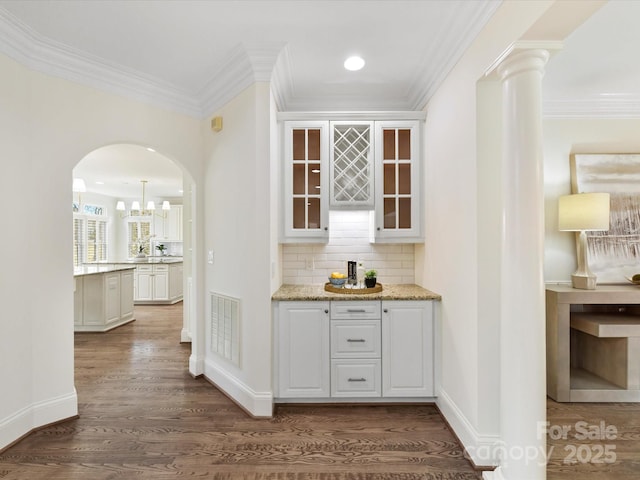 bar featuring visible vents, backsplash, ornamental molding, arched walkways, and dark wood-style floors