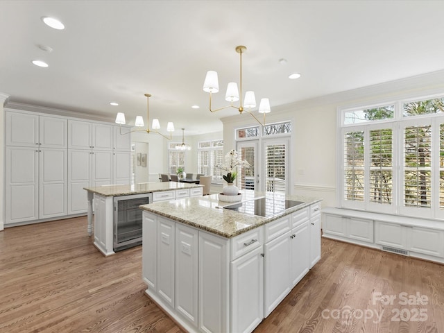 kitchen with beverage cooler, a center island, white cabinets, black electric cooktop, and a chandelier