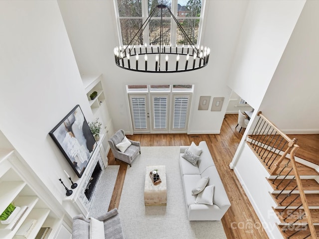 living room featuring wood finished floors, stairway, an inviting chandelier, baseboards, and a towering ceiling