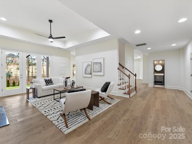 living area with stairway, wood finished floors, visible vents, a tray ceiling, and recessed lighting